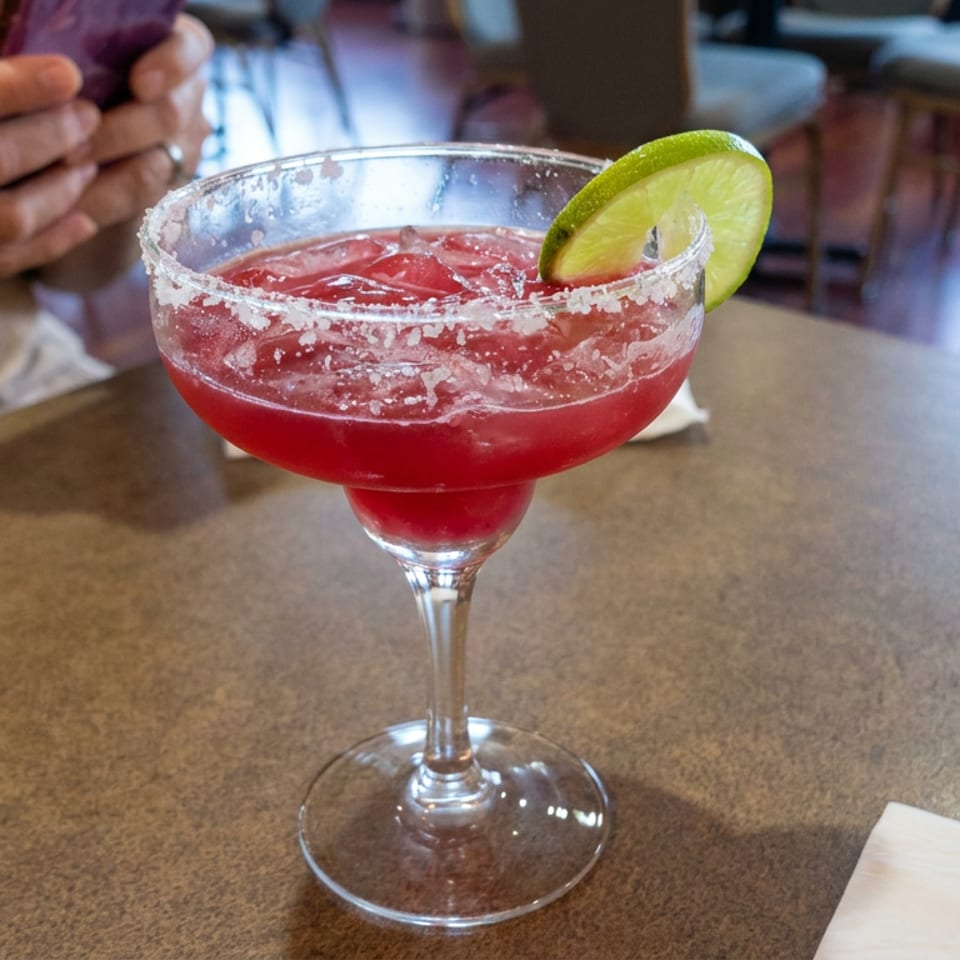 Red margarita with a salted rim and lime garnish served in a stemmed glass on a restaurant table.